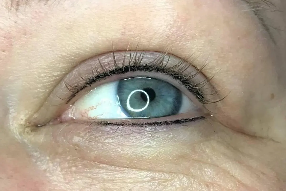 Healed eyeliner tattoo, a fine dark line following the upper and lower lash lines.
